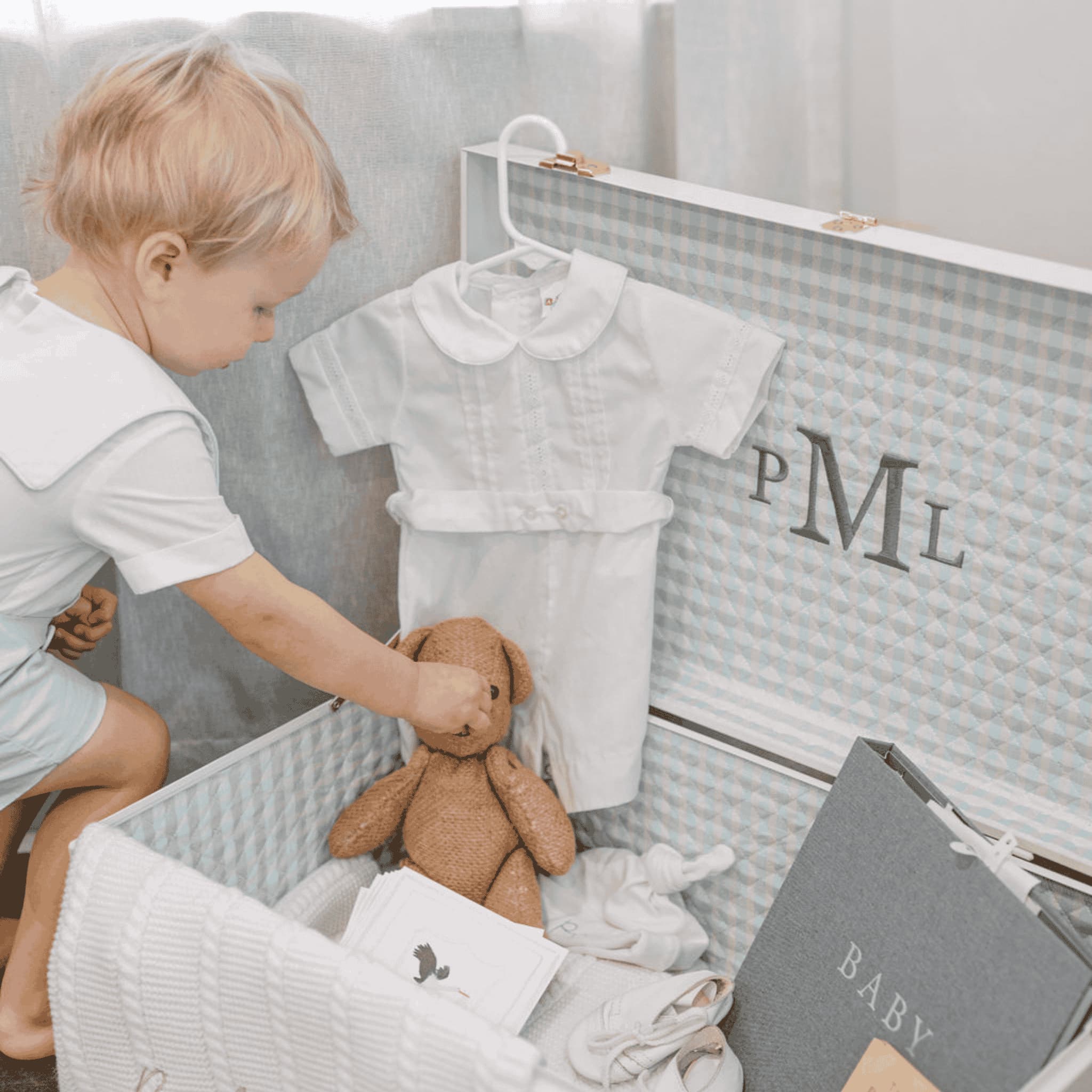 Child playing with a teddy bear in a crib with baby clothes and a book.