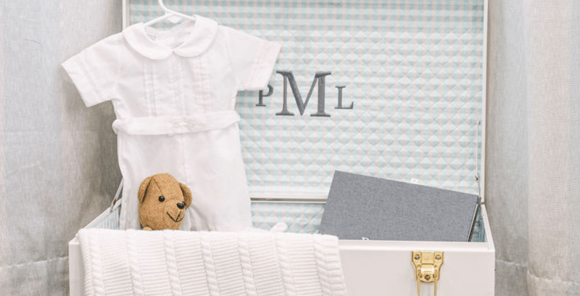 White baby outfit with a teddy bear and gray book in a white box, monogrammed 'PML' on a light gray background.