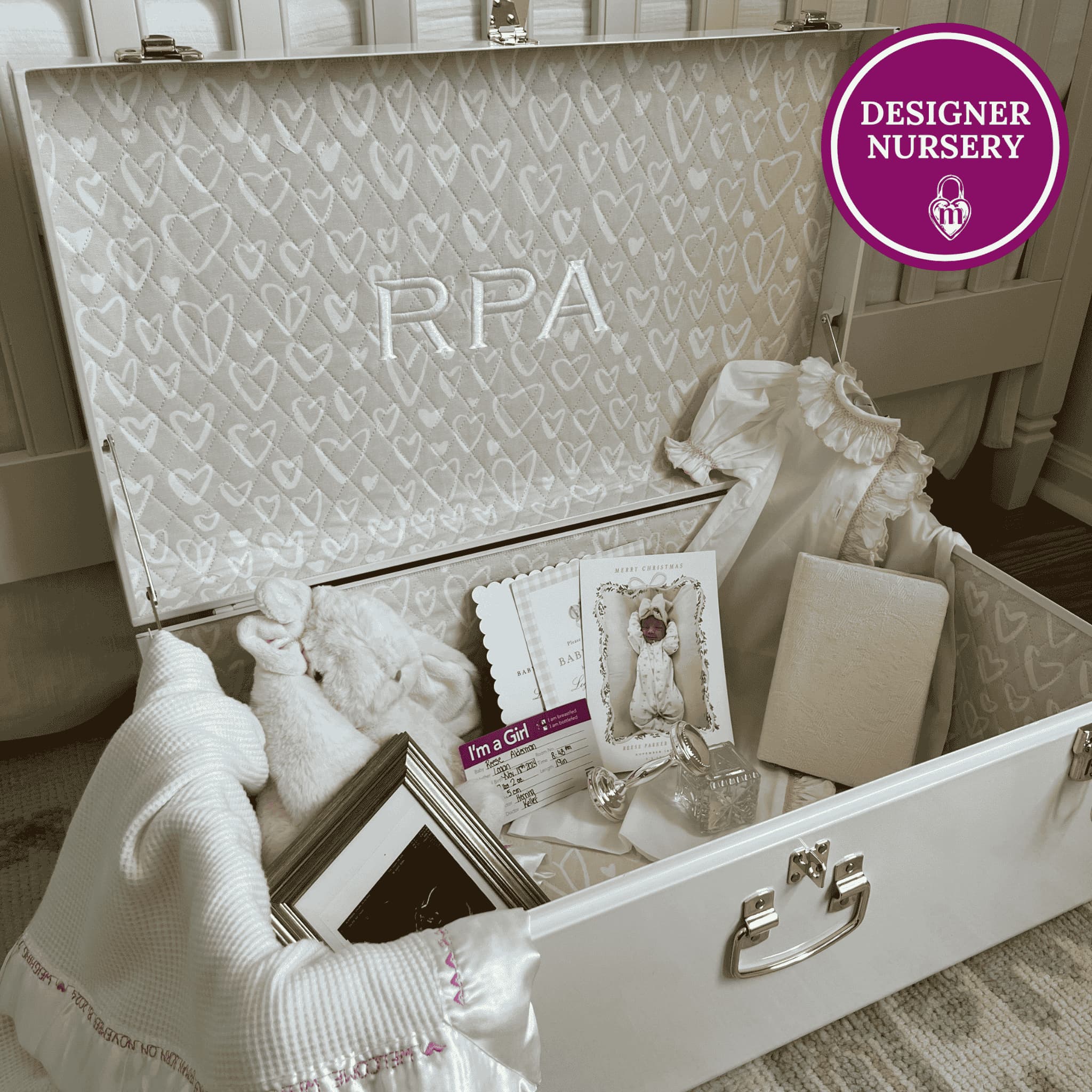 Open memory box with baby items and 'RPA' monogram, branded 'Designer Nursery' in top right corner.