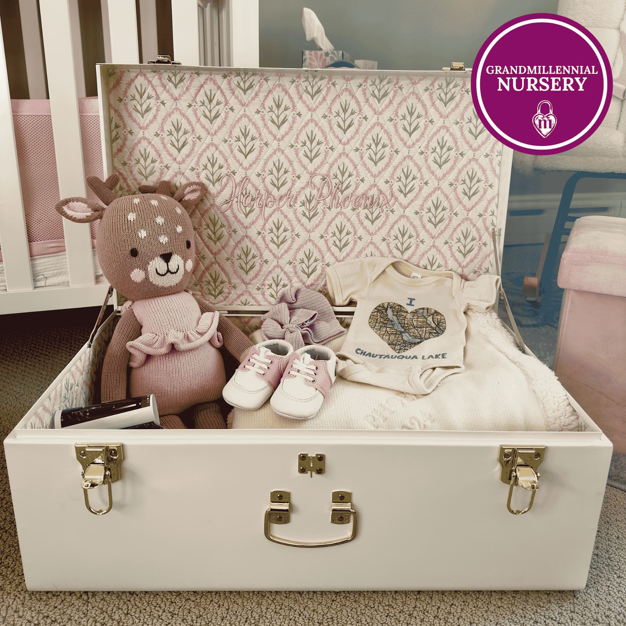 White keepsake trunk with baby items including a teddy bear, shoes, and a bag in a nursery setting.
