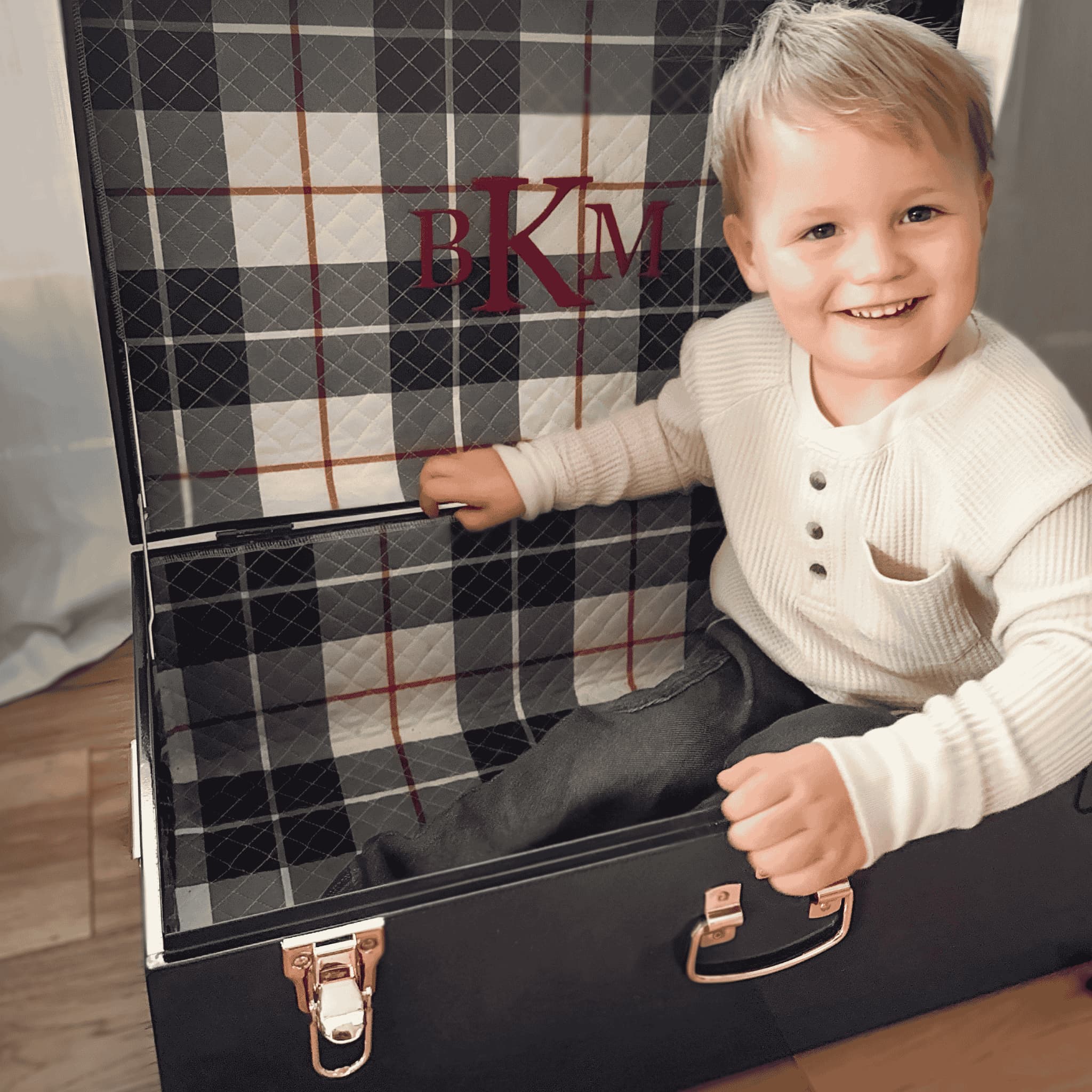 Child sitting inside a navy keepsake trunk with plaid interior, smiling.